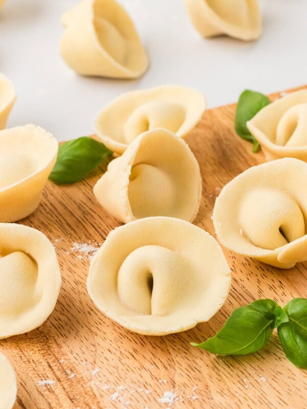 Freshly shaped gluten-free tortellini arranged on a wooden board with fresh basil leaves