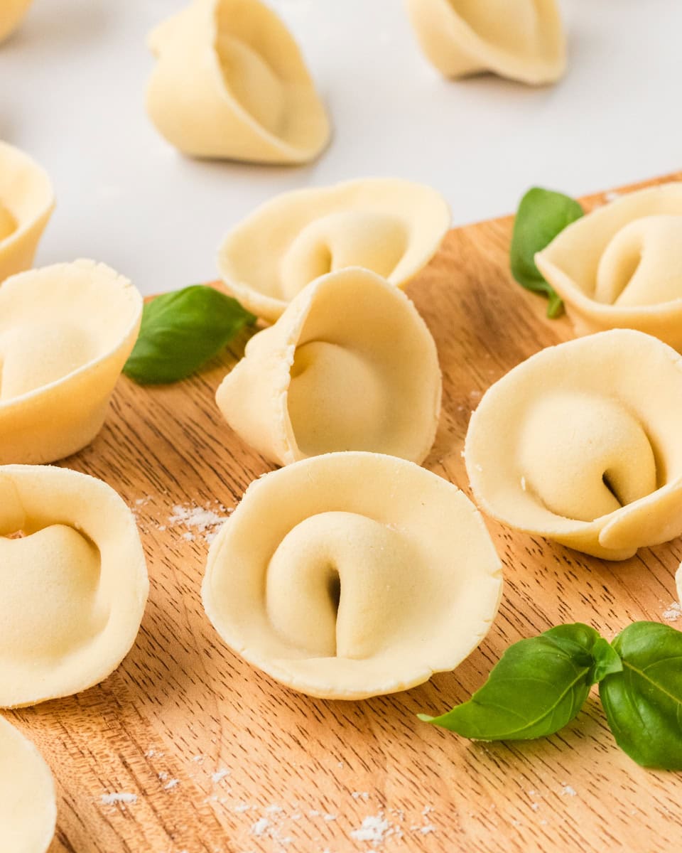 Freshly shaped gluten-free tortellini arranged on a wooden board with fresh basil leaves