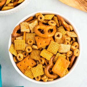 Overhead view of a white bowl filled with gluten-free Chex Mix including pretzels, Chex cereals, O’s cereal, and square cheese crackers.