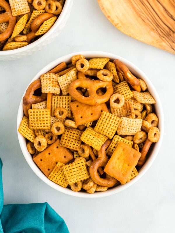 Overhead view of a white bowl filled with gluten-free Chex Mix including pretzels, Chex cereals, O’s cereal, and square cheese crackers.