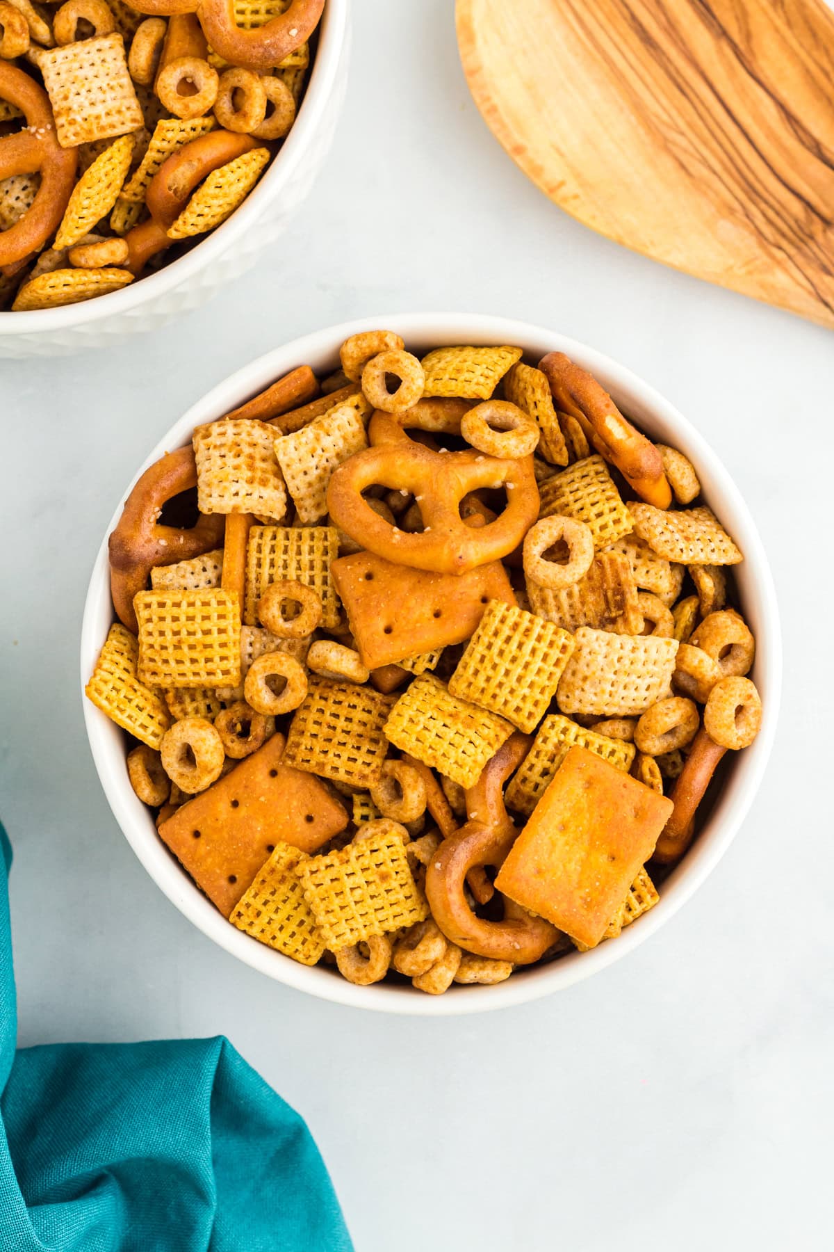 Overhead view of a white bowl filled with gluten-free Chex Mix including pretzels, Chex cereals, O’s cereal, and square cheese crackers.