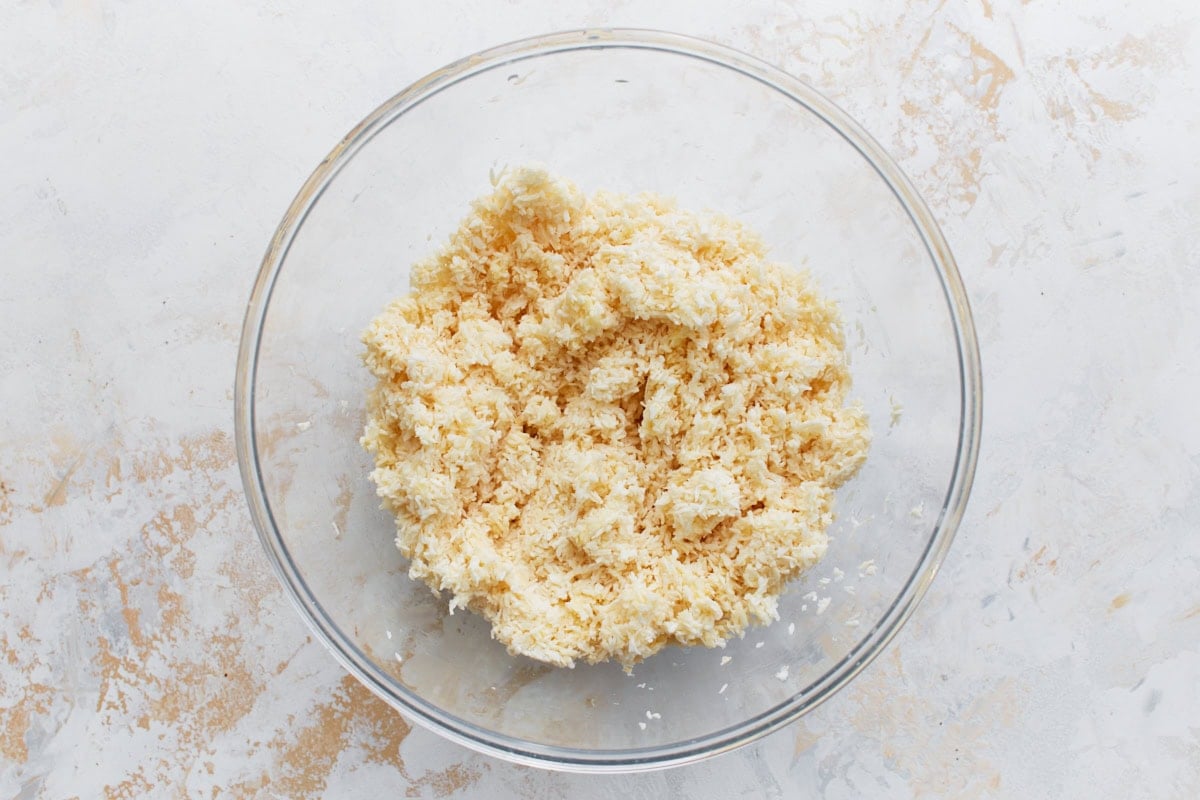 Large mixing bowl filled with shredded sweetened coconut, egg whites, and melted butter for the crust mixture.