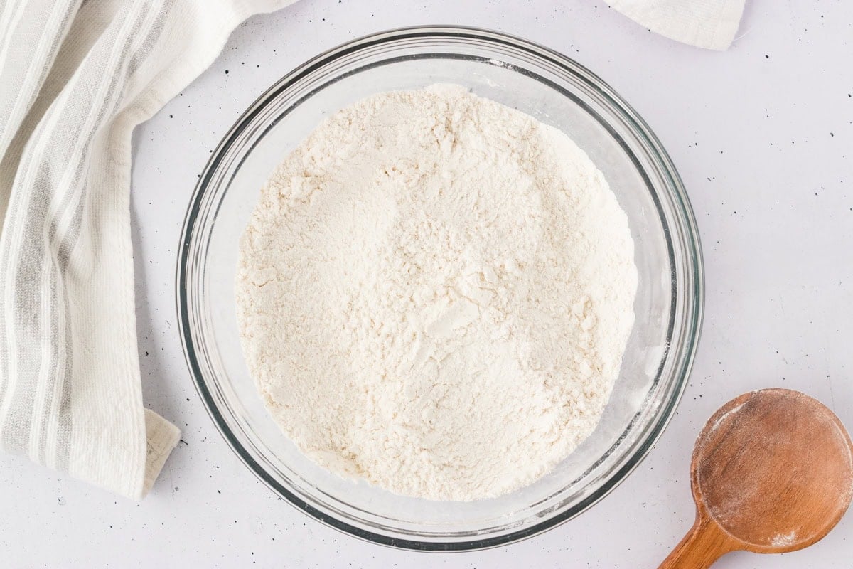 Overhead view of a clear glass bowl filled with gluten-free flour mixture on a white countertop.