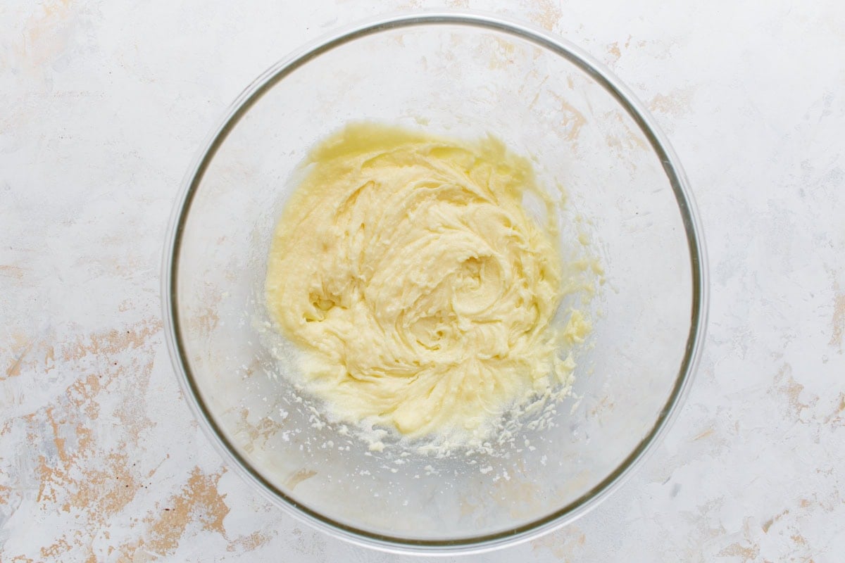 Glass mixing bowl with a light, fluffy mixture of creamed butter and sugar, shown from overhead on a neutral background.