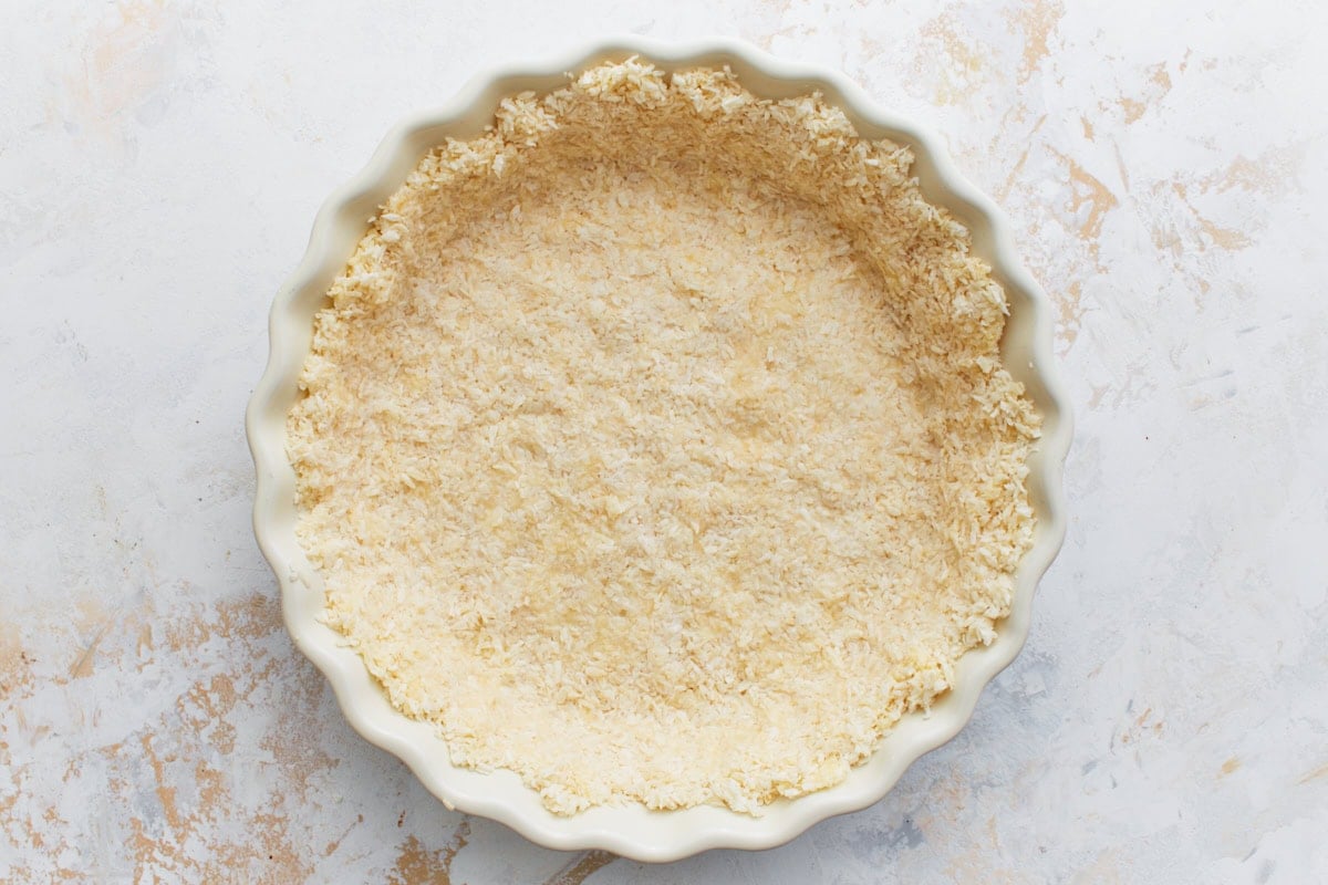 Unbaked coconut crust mixture pressed evenly into a fluted pie dish.