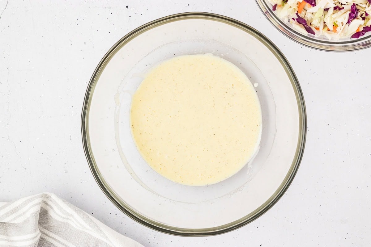 Overhead view of the completed creamy coleslaw dressing fully whisked in a glass bowl, ready for mixing.