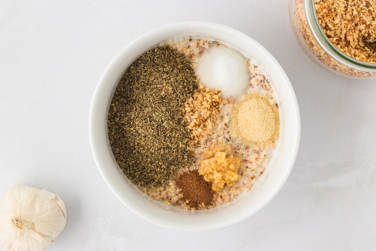 White bowl filled with gluten-free breadcrumbs, dried Italian herbs, garlic, onion powder, and other seasonings for the meatball mixture.