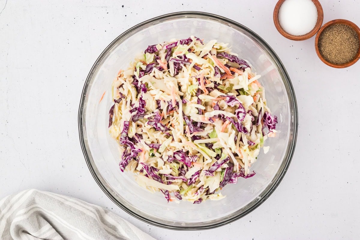 A large glass bowl filled with shredded green and purple cabbage and carrots just after being tossed with the dairy-free dressing.