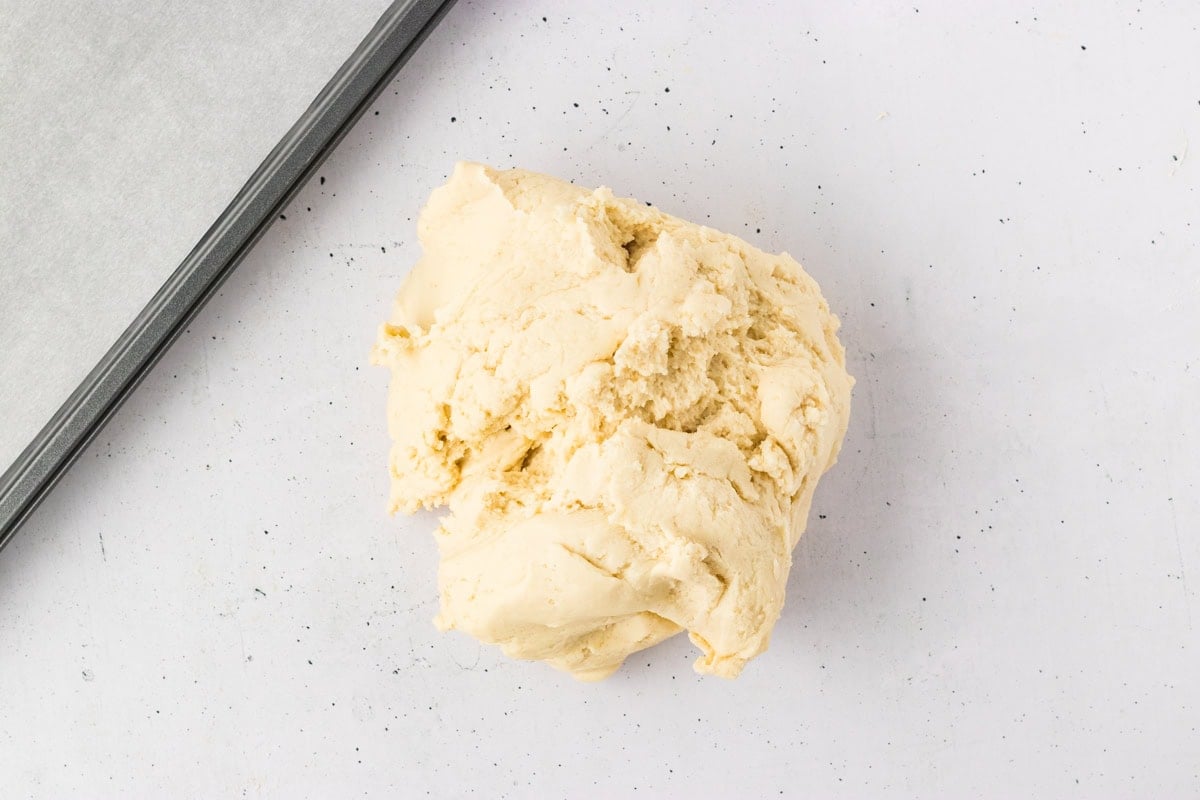 Portion of gluten-free breadstick dough placed on a lightly floured surface next to a baking tray.