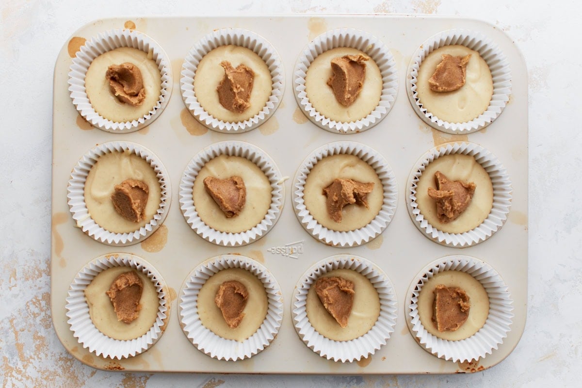 Muffin tin with batter topped by spoonfuls of cinnamon sugar mixture, not yet swirled in.