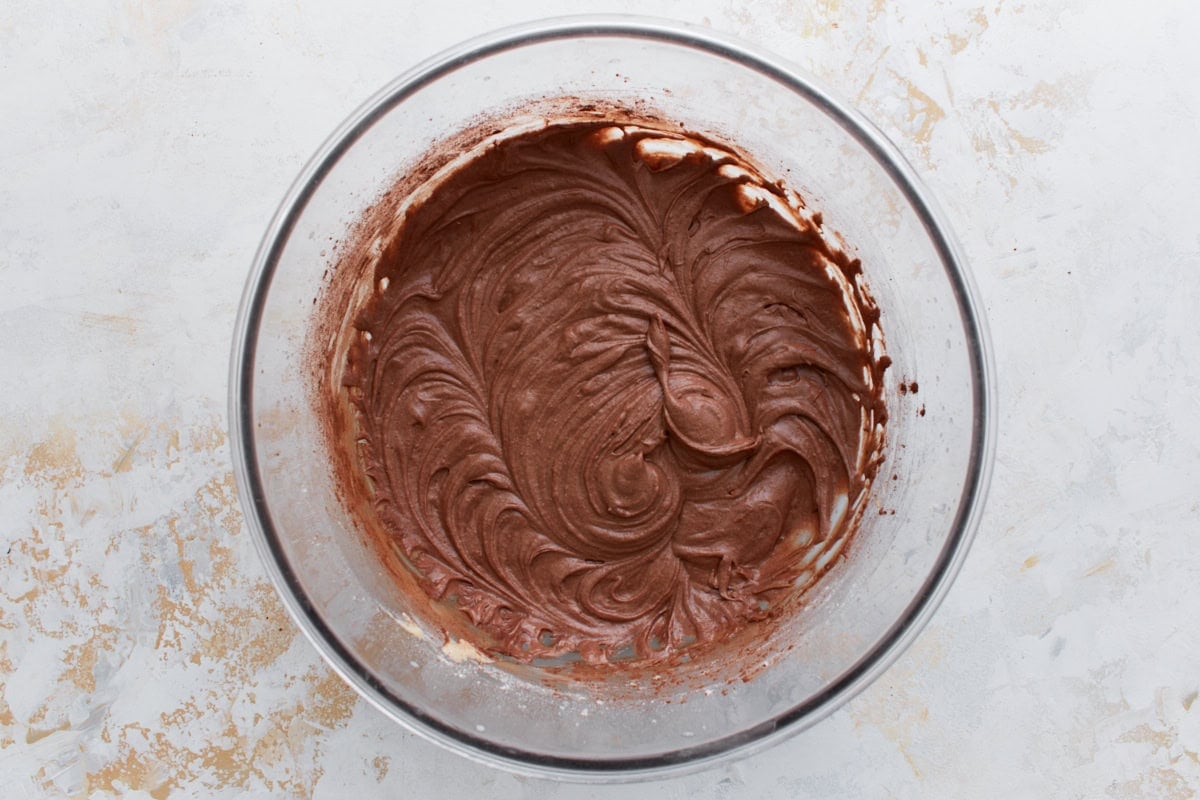 Smooth, rich chocolate cupcake batter swirled in a glass mixing bowl after cocoa powder has been added.