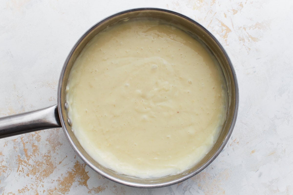 Custard mixture in a saucepan beginning to thicken as it cooks.