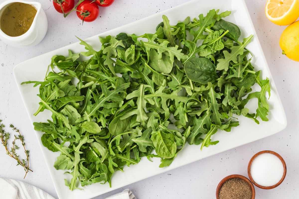 Fresh arugula and spinach mix laid out on a white rectangular platter, ready to be topped for Tuna Nicoise Salad.