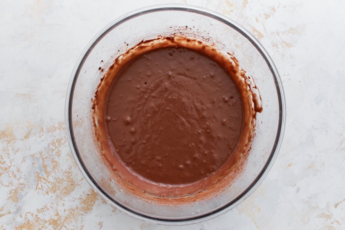 Glossy, pourable chocolate batter in a bowl after boiling water is added, with bubbles forming on the surface.
