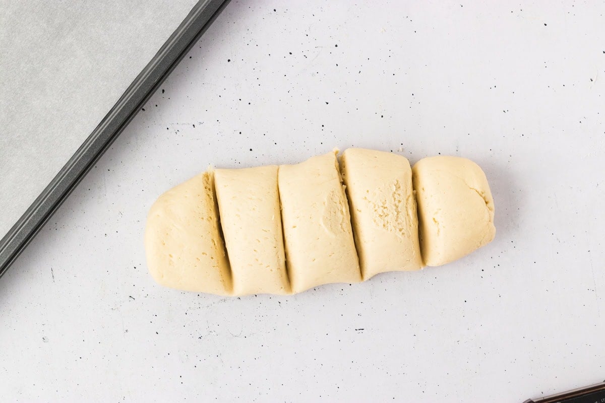 Gluten-free breadstick dough divided into six even pieces on a white counter.