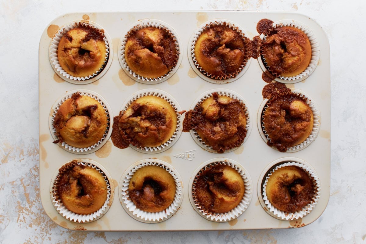 Freshly baked gluten-free cinnamon roll muffins still in the tin, showing golden brown tops with caramelized cinnamon swirls.