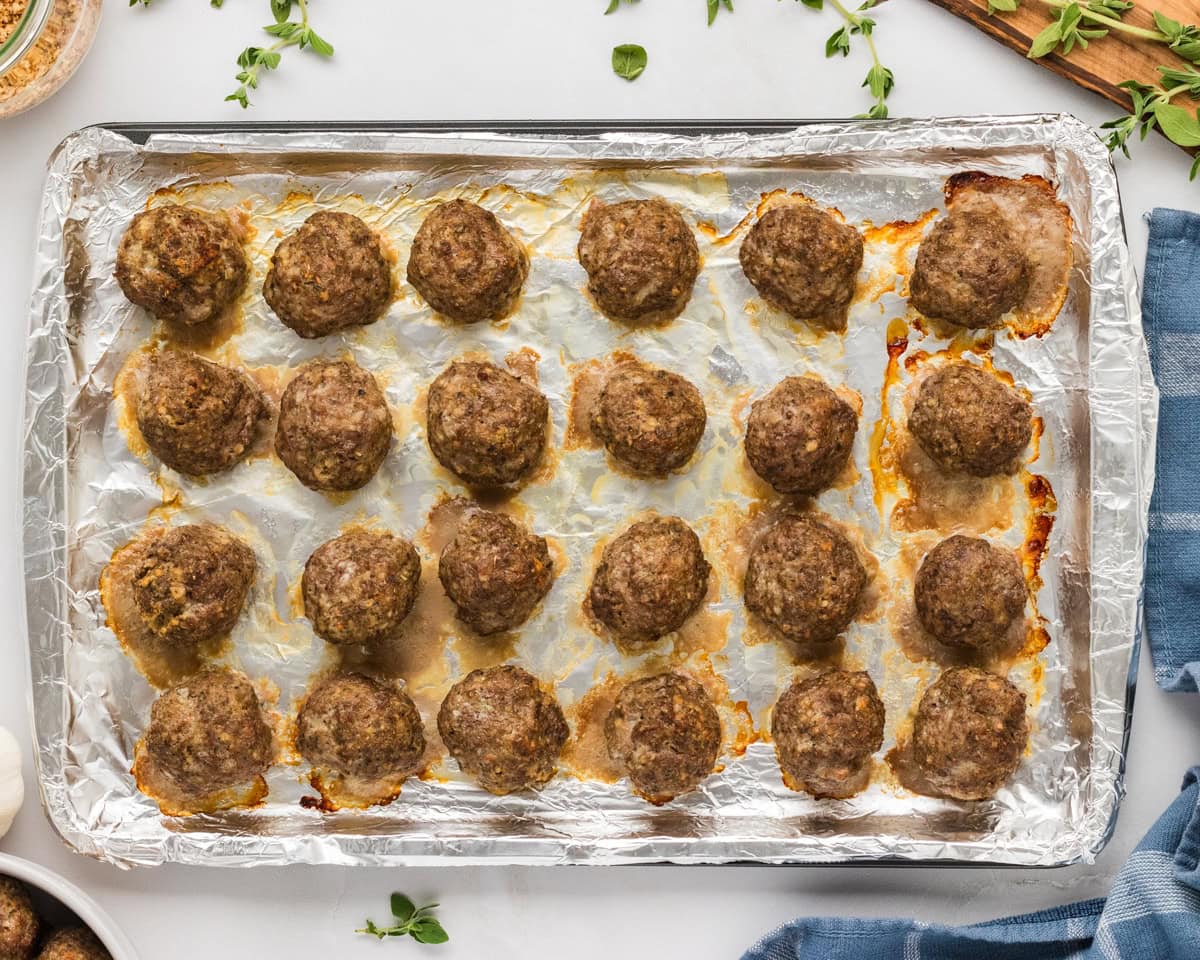 Freshly baked gluten-free meatballs on a foil-lined sheet pan, golden and cooked through.