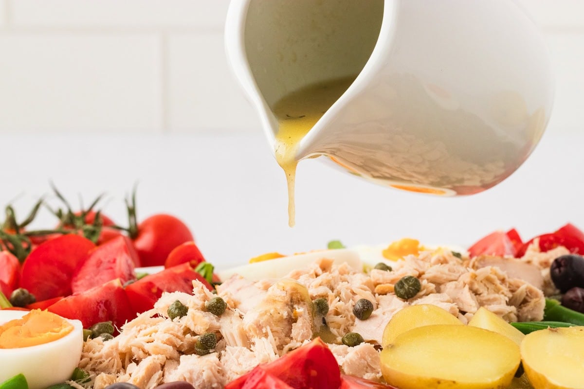 Close-up of vinaigrette being poured over the center of the Tuna Nicoise Salad, highlighting capers, tuna, and potatoes.