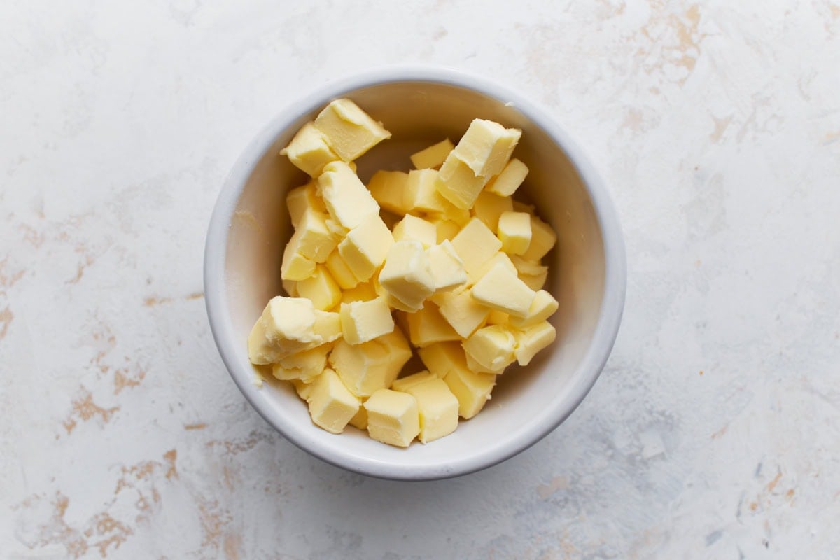 A white bowl filled with small cubes of cold butter, ready to be mixed into the biscuit dough.