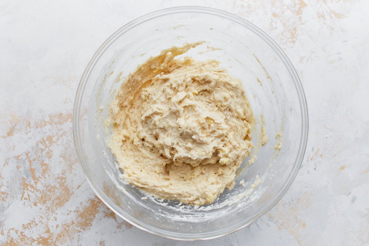 Biscuit dough just mixed, appearing soft and slightly sticky in a clear mixing bowl.