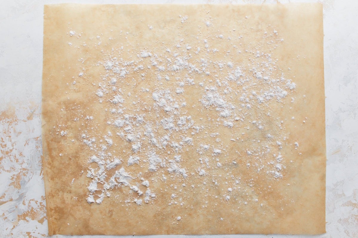 Parchment paper lightly dusted with gluten-free flour, prepared as a surface for shaping biscuit dough.