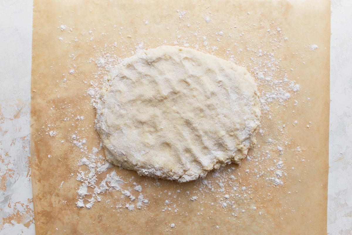 xFlattened biscuit dough formed into a round disk on the floured parchment paper.
