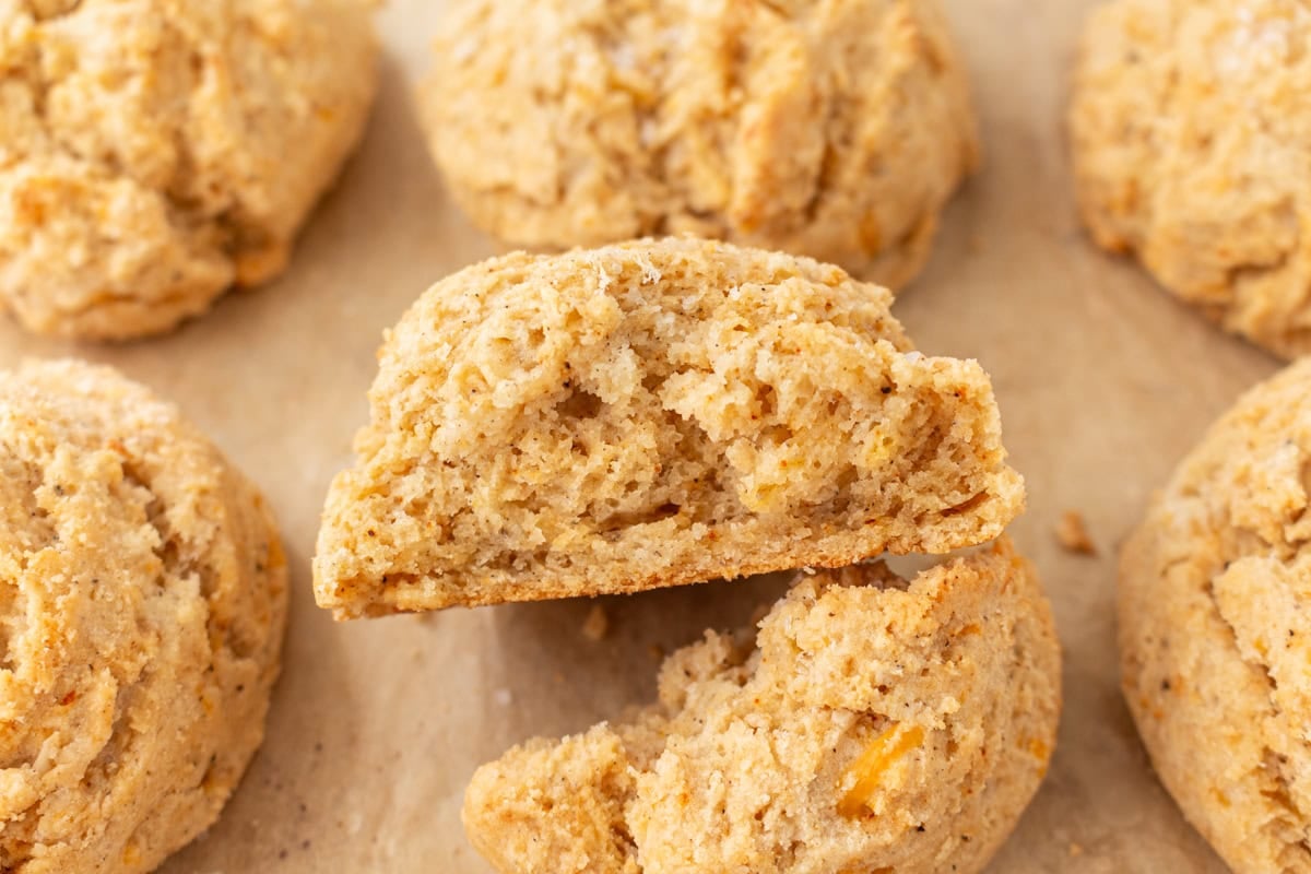 A close-up of a biscuit broken in half, showing the tender, fluffy interior with visible cheese bits.