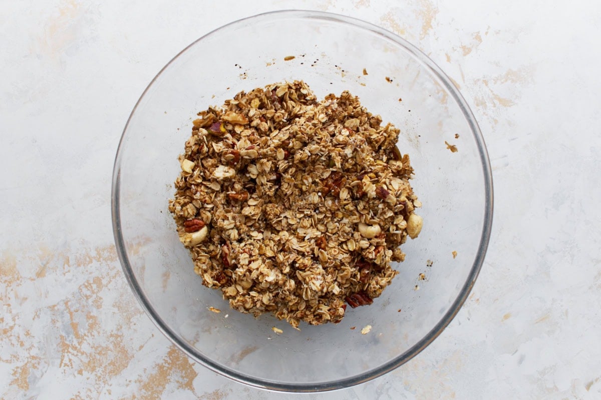 The same mixing bowl now filled with fully mixed granola ingredients, including oats and nuts coated in a wet mixture.