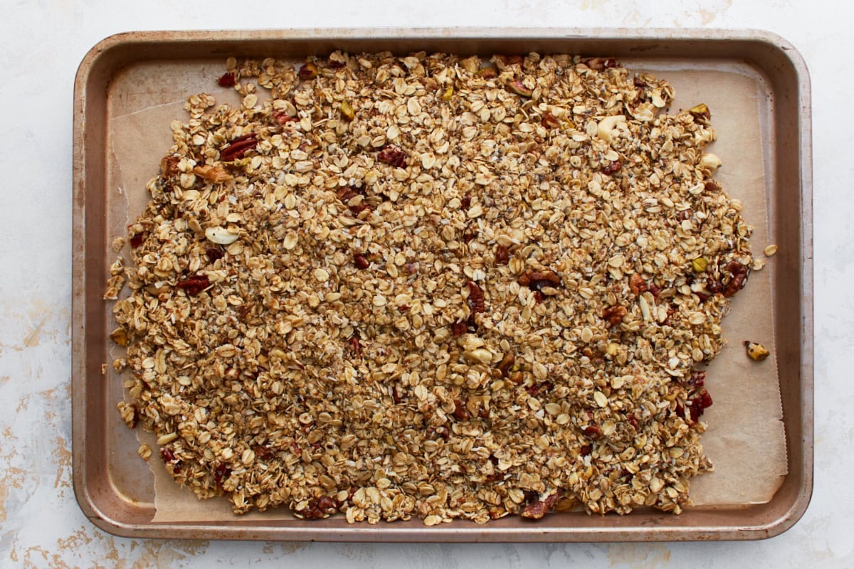 An overhead view of the granola mixture spread out evenly on a parchment-lined baking sheet before going into the oven.