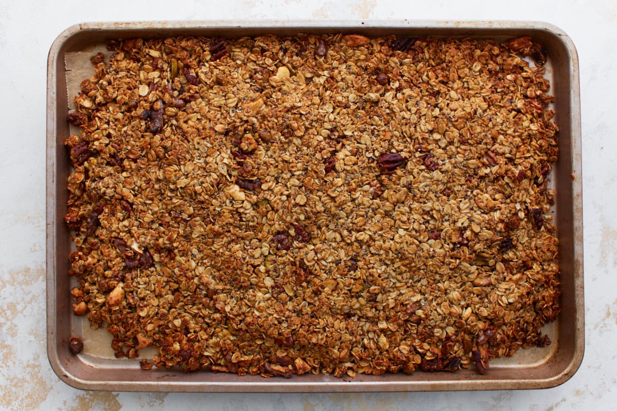Baked granola straight from the oven, evenly golden and still spread out flat on the baking sheet.