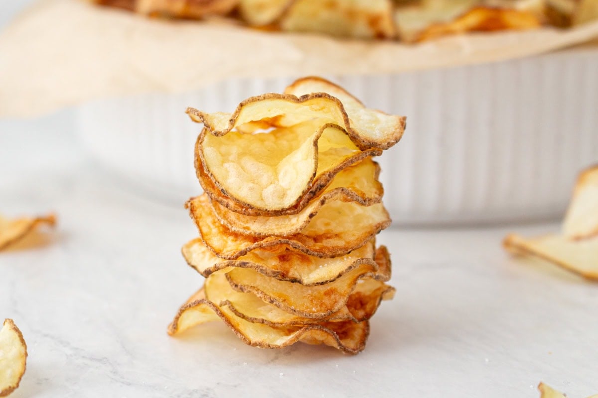 Stack of crispy potato chips showing their airy, wavy texture on a white marble surface.