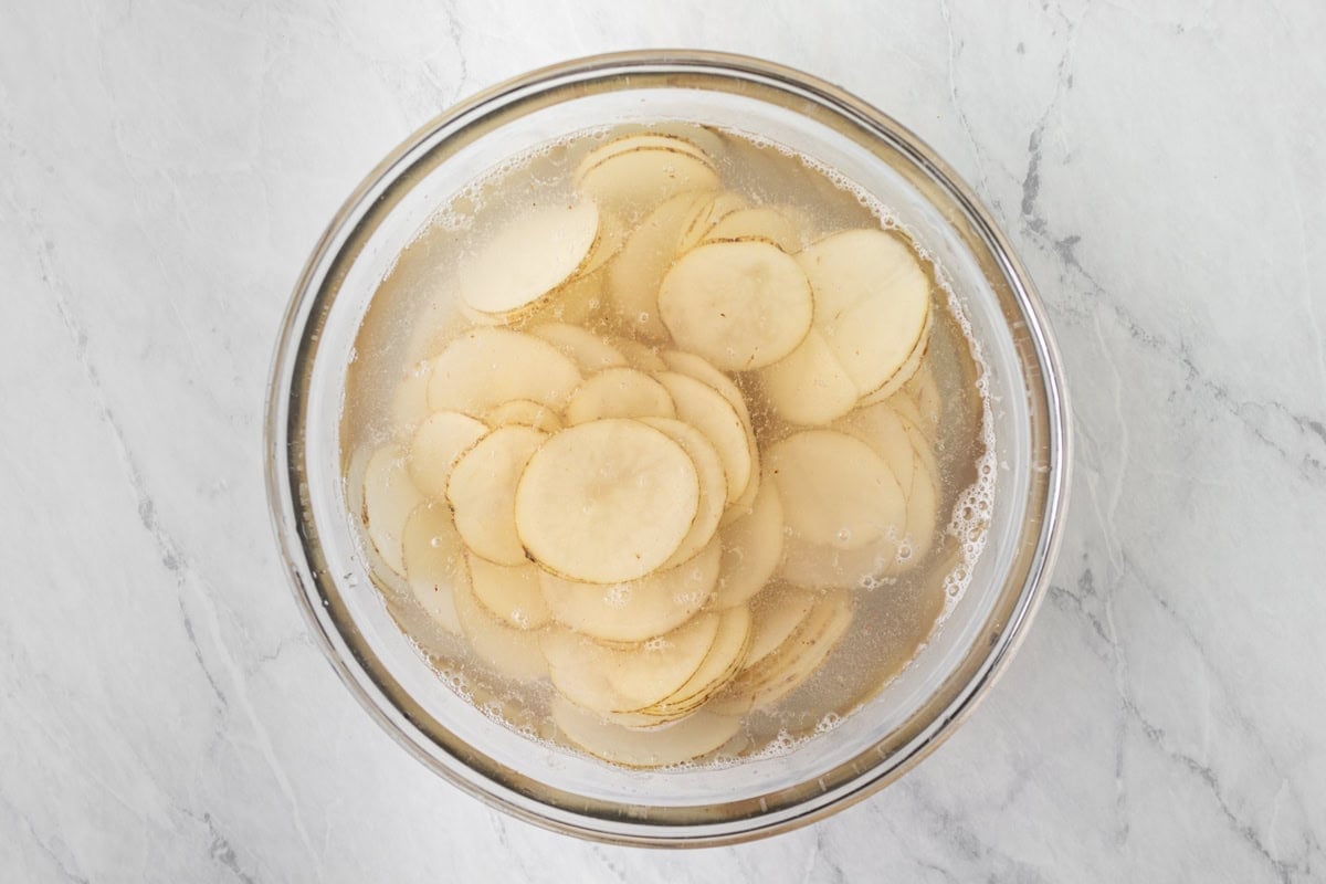 Potato slices soaking in a bowl of water and vinegar to remove excess starch.
