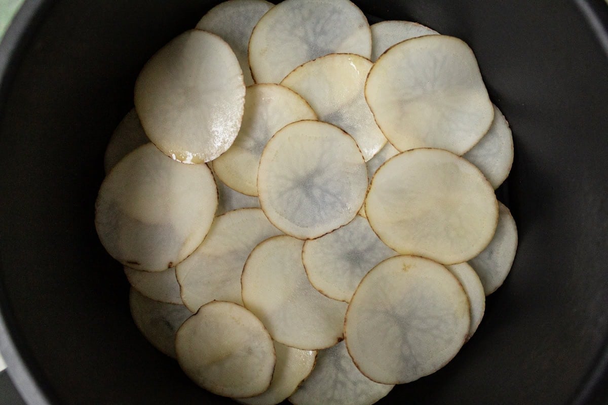 Potato slices arranged in overlapping layers in the air fryer basket before cooking.