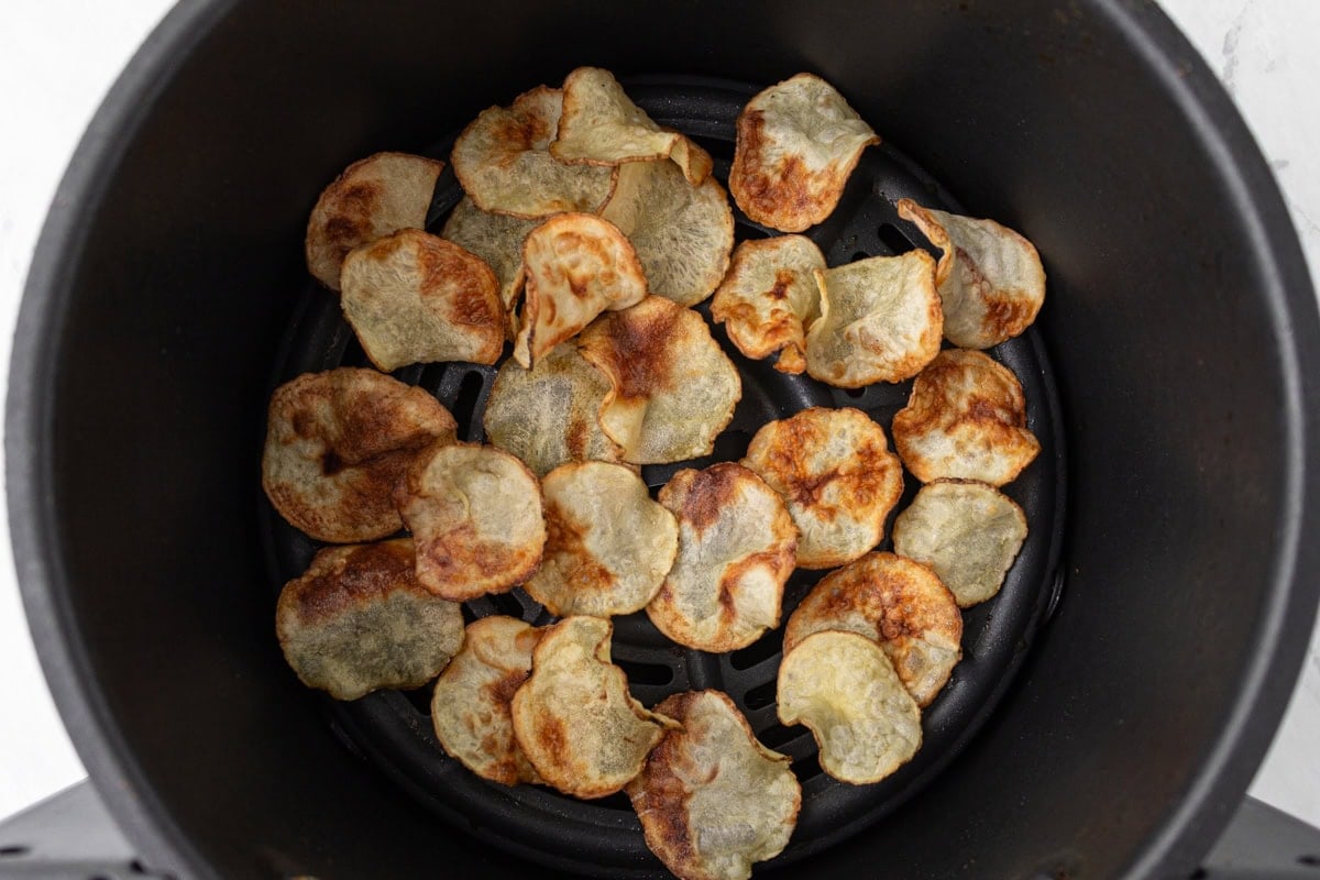 Cooked potato chips in the air fryer basket, golden and slightly curled at the edges.