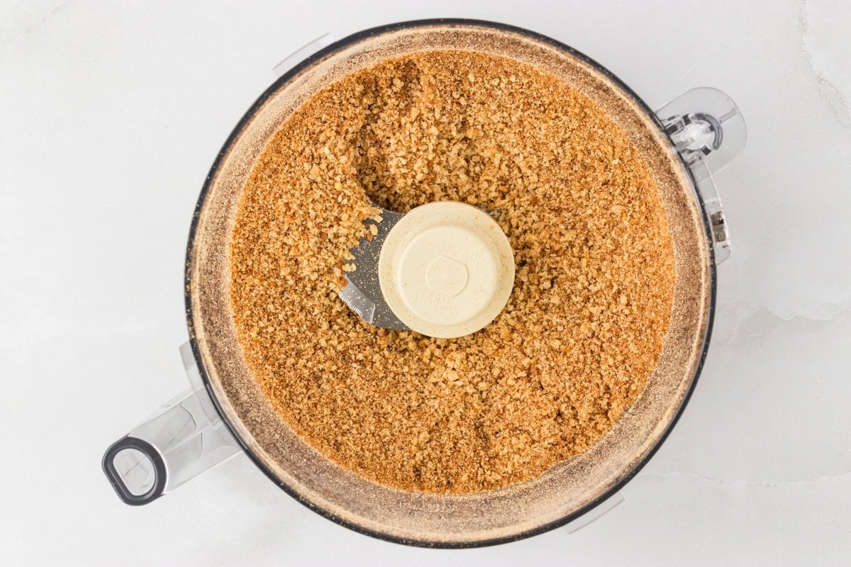 Top-down view of finely ground gluten-free breadcrumbs inside a food processor after blending.
