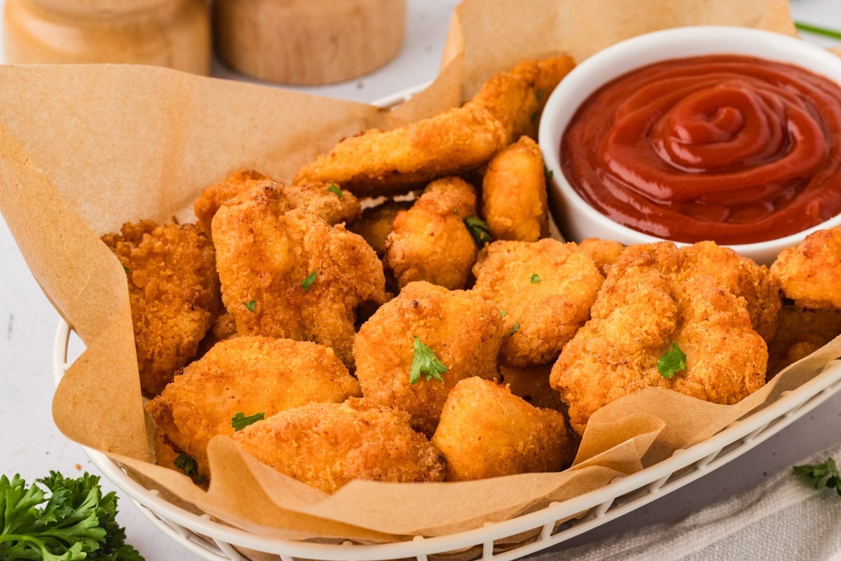 Basket of baked gluten-free chicken nuggets lined with parchment paper, served with ketchup, ready to eat.