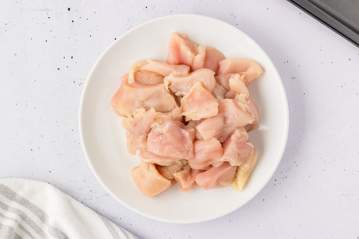Plate of raw, diced chicken breast cut into nugget-sized pieces, ready for coating.