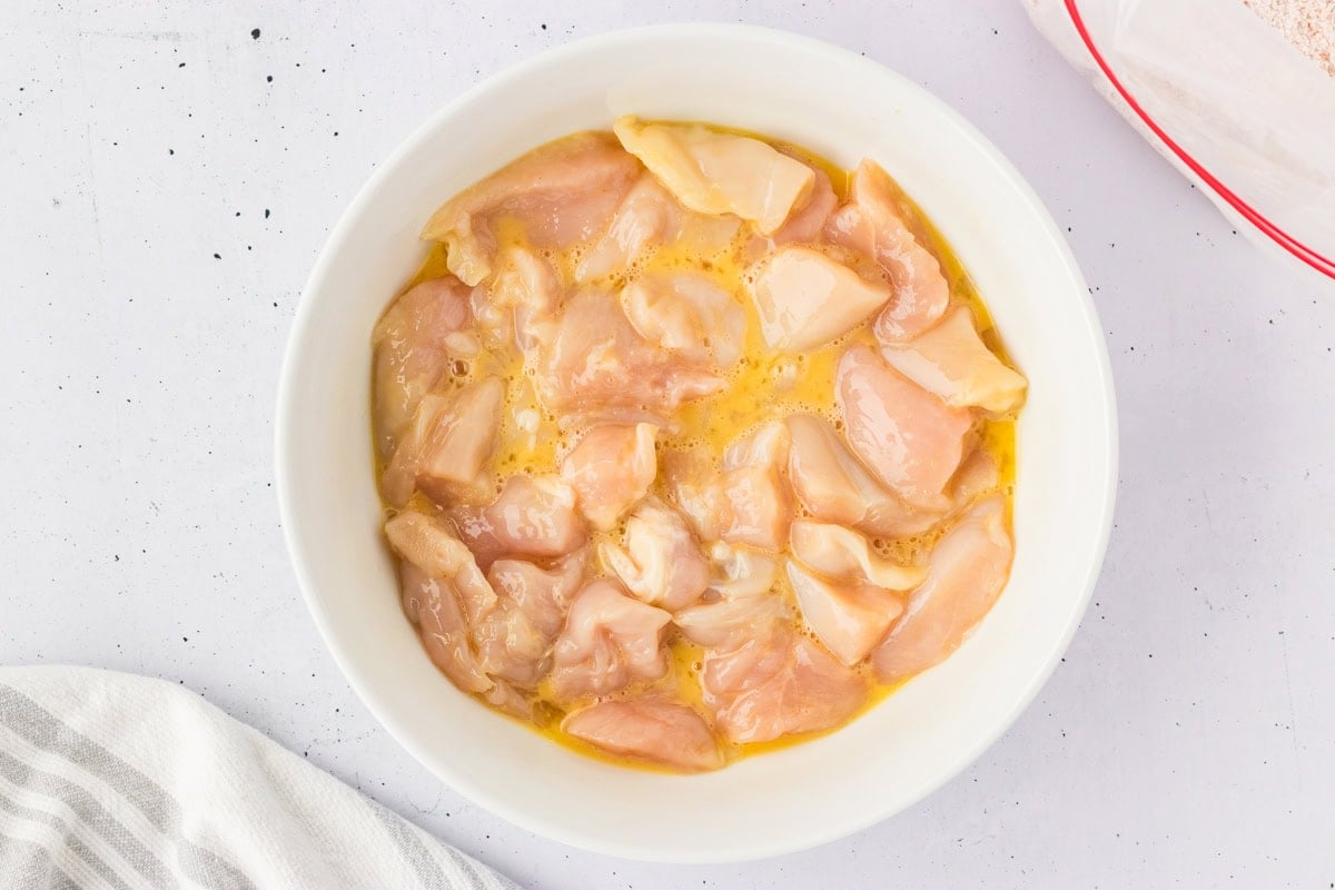 Bowl of chicken nugget pieces coated in beaten egg, prepped for breading.