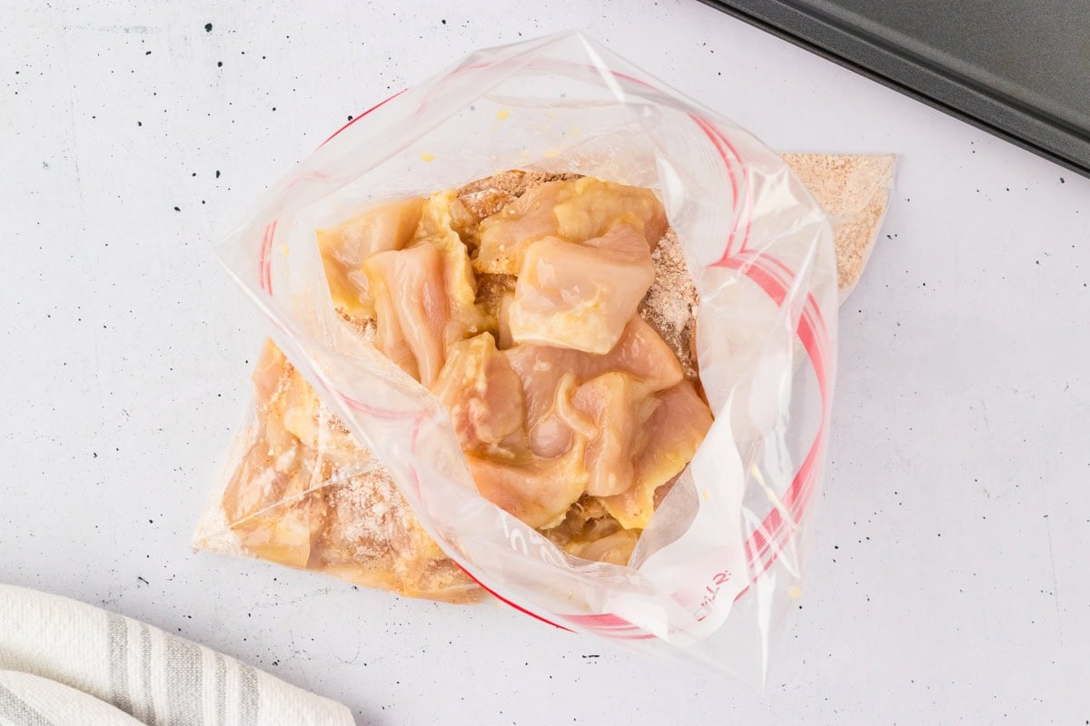 Raw chicken pieces added to the bag of seasoned flour mix, ready to be coated.
