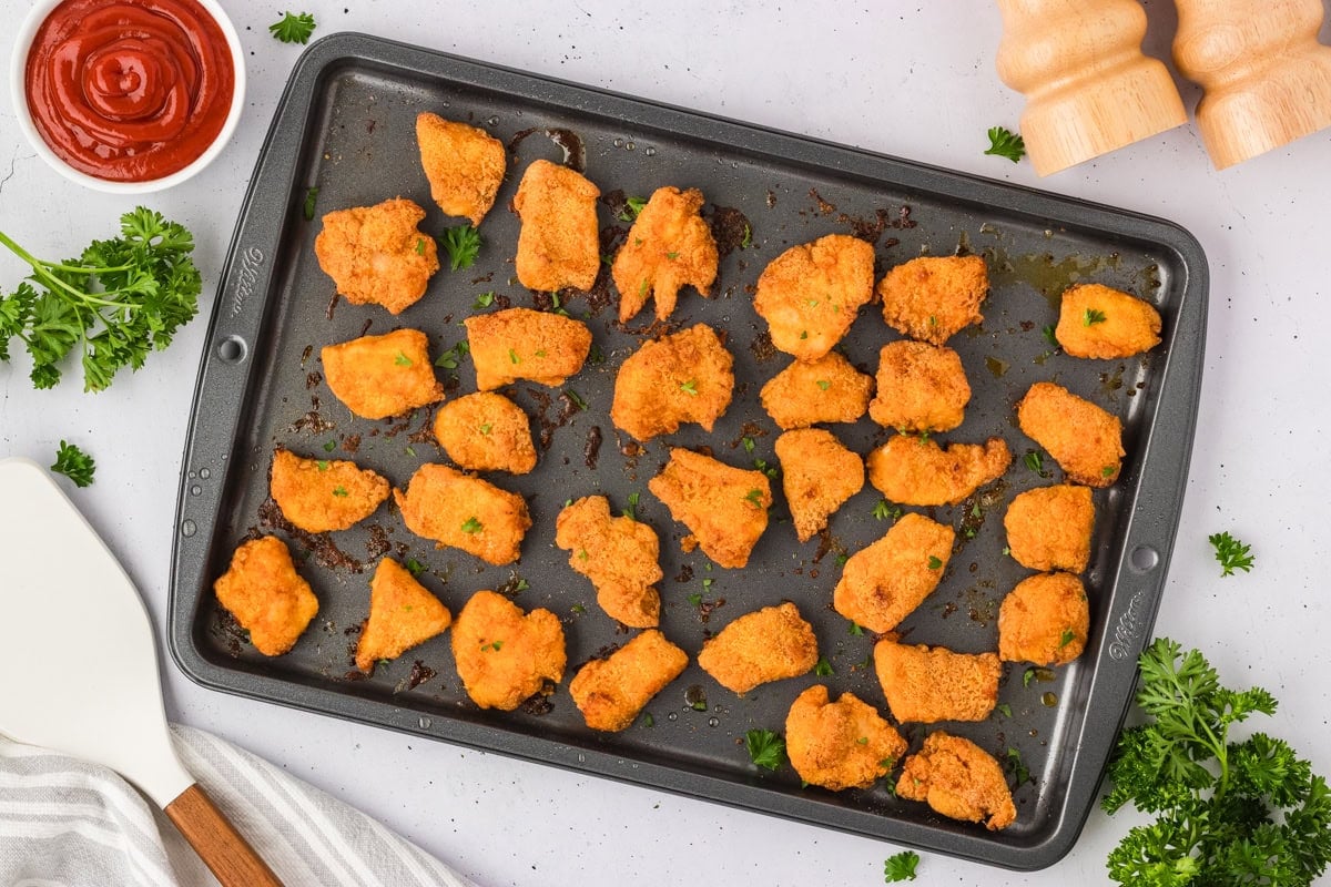 Freshly baked gluten-free chicken nuggets on a baking sheet, golden brown and garnished with chopped parsley.