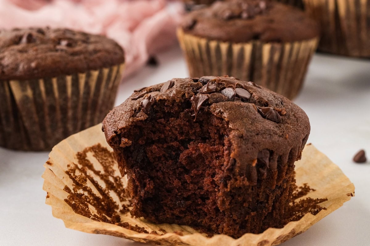 Close-up of a bitten-into chocolate muffin, showing a rich, moist crumb and gooey melted chocolate chips.