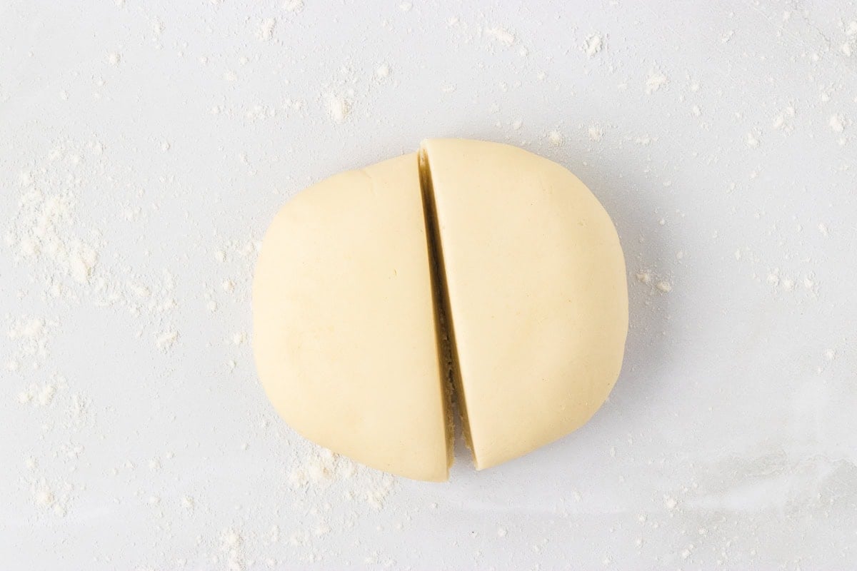 Rested dough ball cut in half on a lightly floured surface