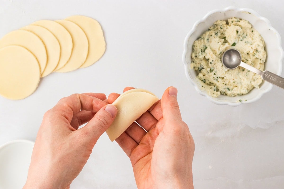 Folding a pasta round in half to seal the ricotta filling inside for gluten-free tortellini