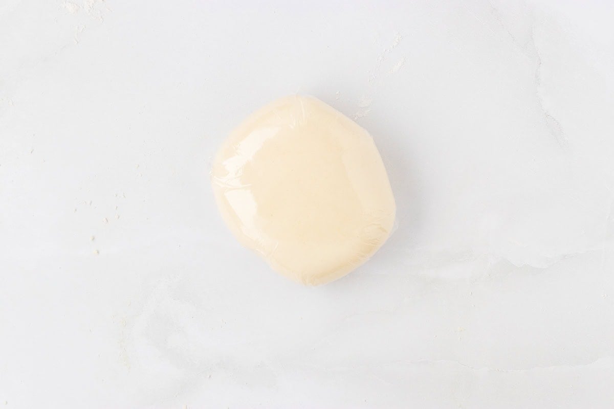Gluten-free pasta dough wrapped tightly in plastic wrap on a white surface