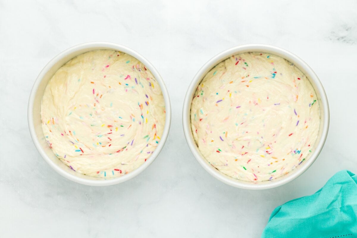 Two 8-inch round cake pans filled with funfetti batter, ready for the oven.
