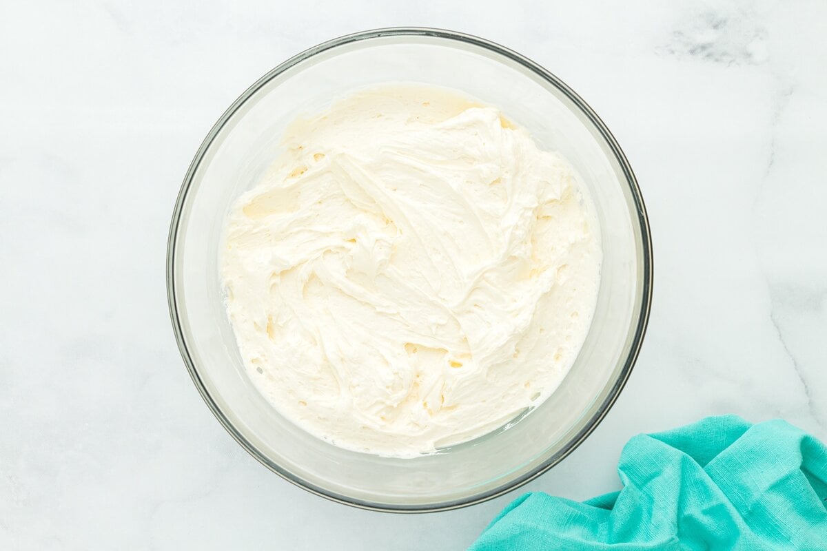 A glass mixing bowl filled with smooth, fluffy vanilla buttercream, ready for frosting the cake.