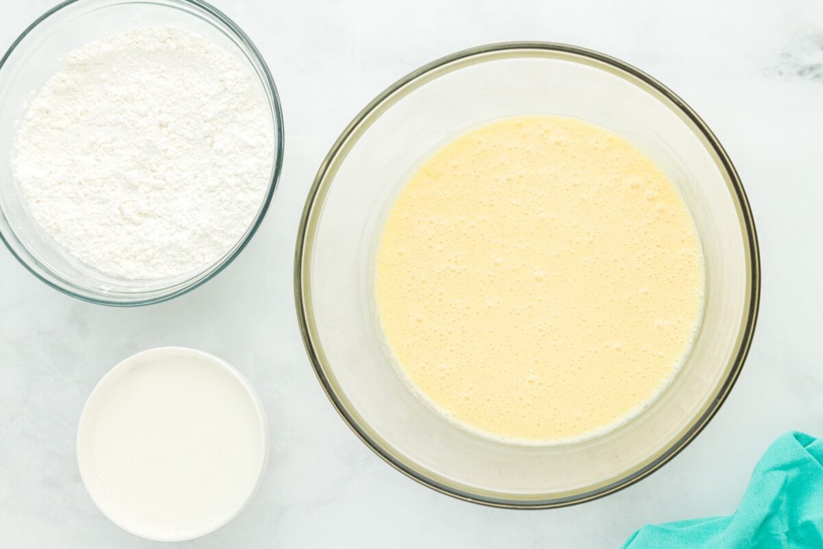 A bowl of whipped wet ingredients next to bowls of gluten-free flour and buttermilk, prepped for combining.