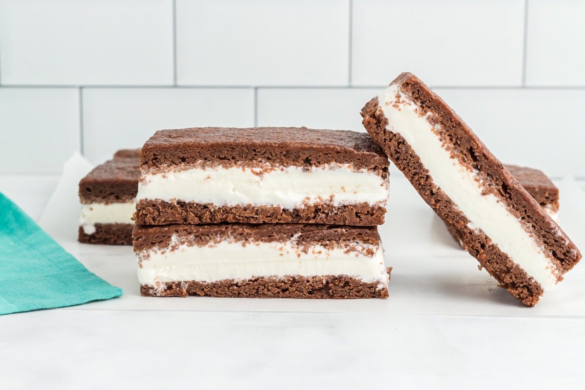Close-up of stacked gluten-free ice cream sandwiches with one sandwich leaning on the others, showing layers of creamy vanilla ice cream between chocolate cookie layers.
