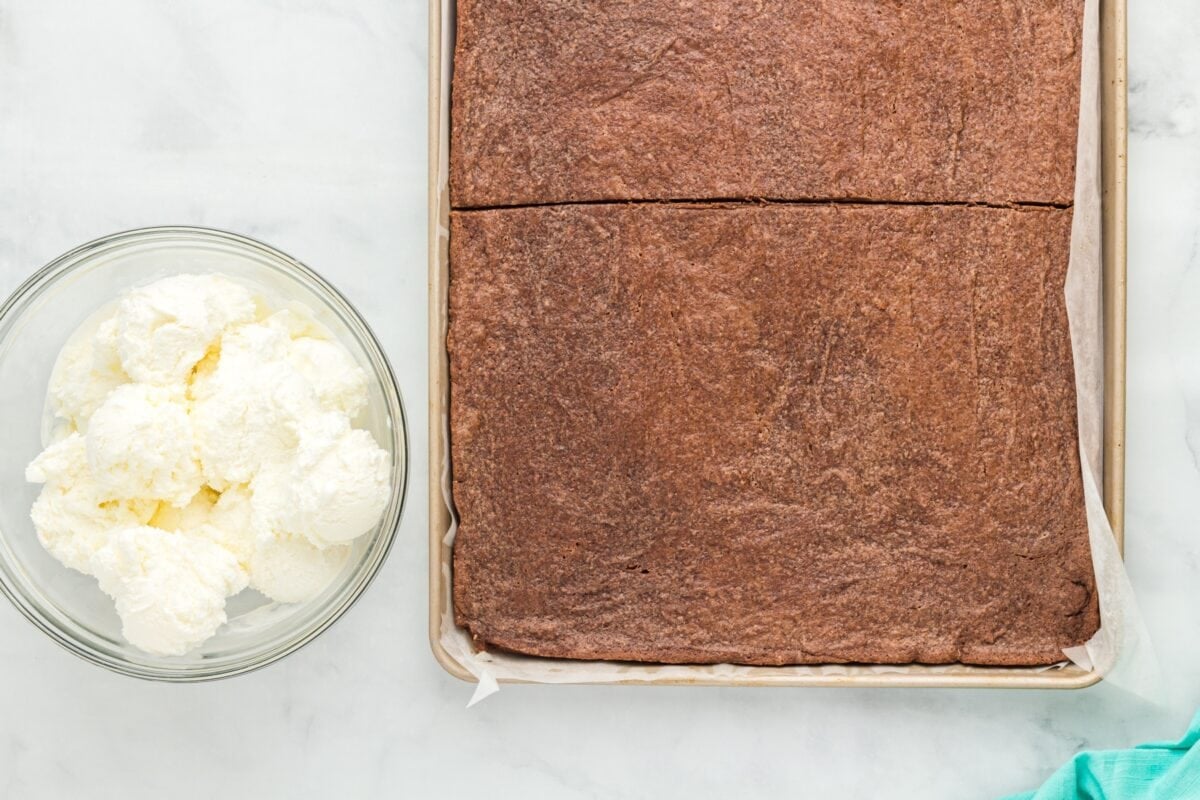 Cookie base cut in half on the baking sheet with a bowl of scooped vanilla ice cream on the side.