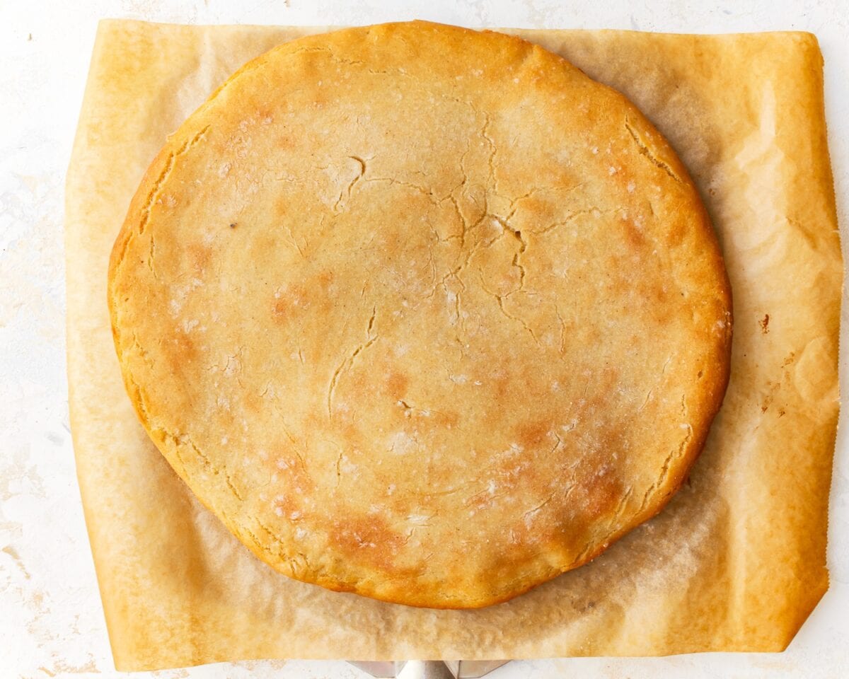 A baked gluten-free pizza crust on parchment paper, golden and firm, ready for toppings.